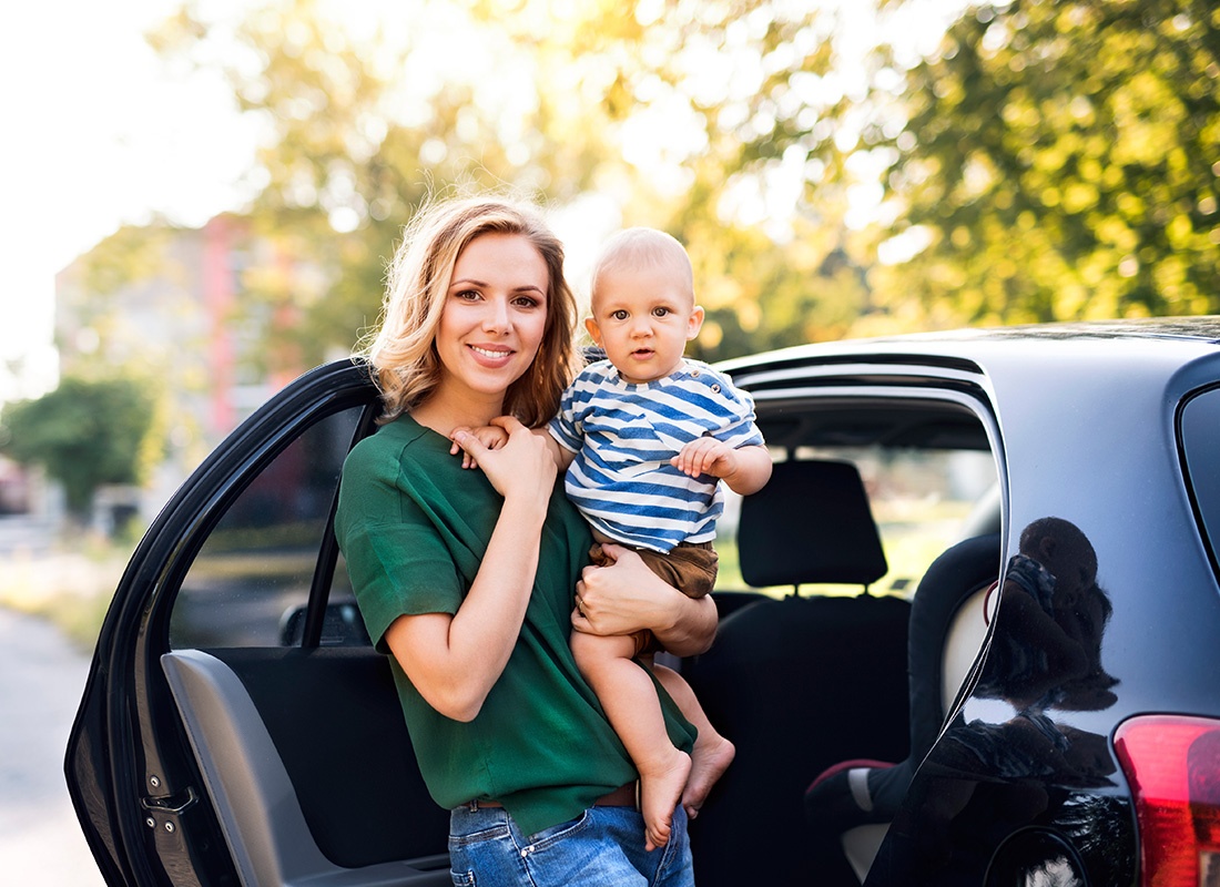 Personal Insurance - Happy Mother Holds Her Baby as She Prepares to Put Him in the Car on a Sunny Day