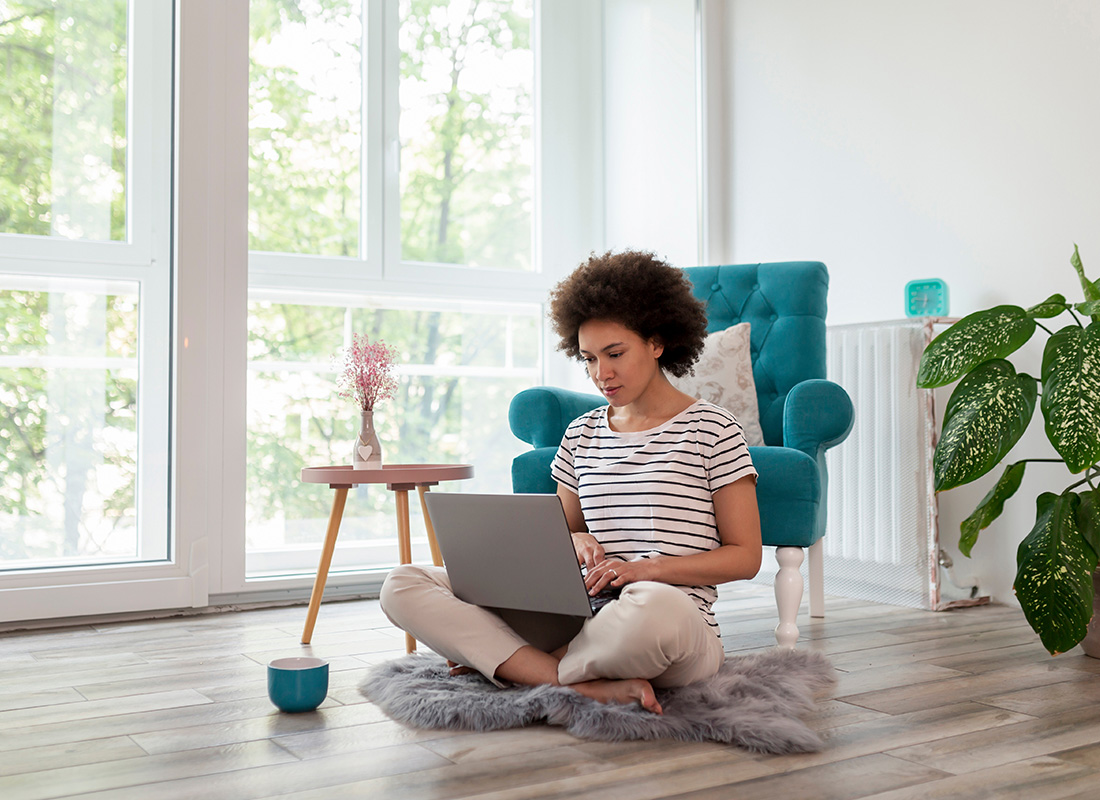 Mortgagee Change Requests - Woman Sitting on a Small Carpet on a Wooden Floor While On Her Computer in Her Home