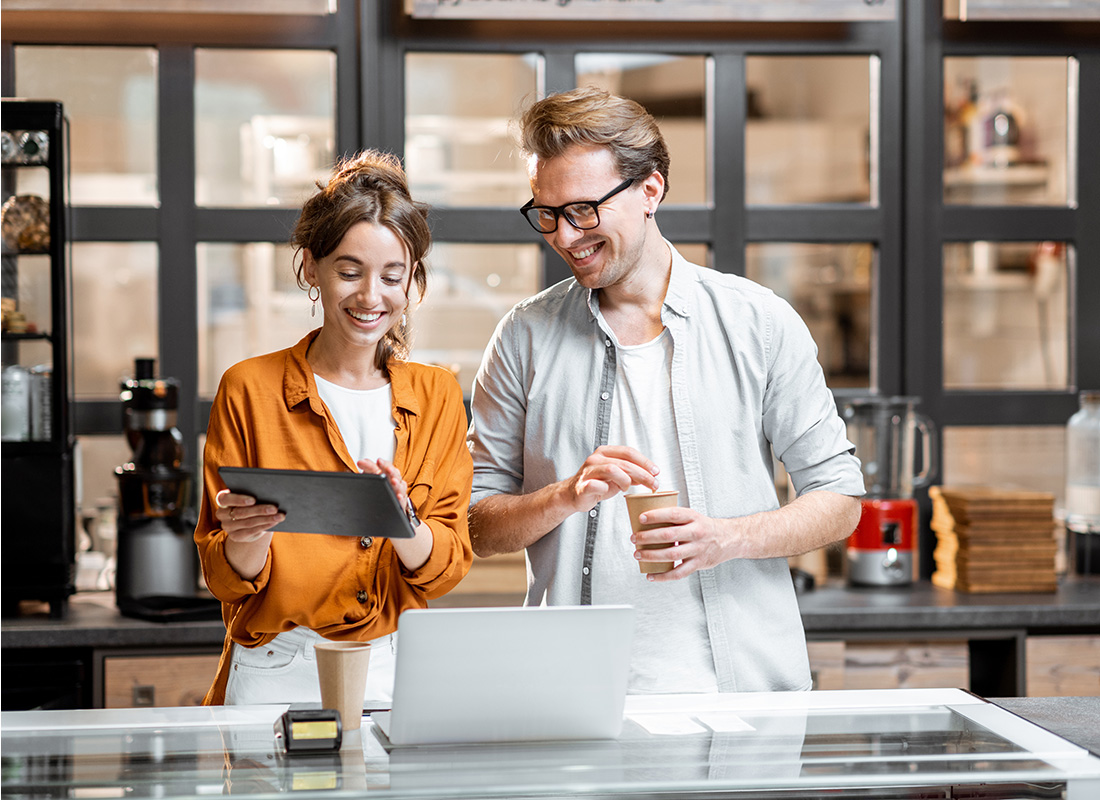 Blog - Cheerful Young Female and Male Small Business Owners Standing Behind the Front Counter of Their Cafe Looking at a Tablet
